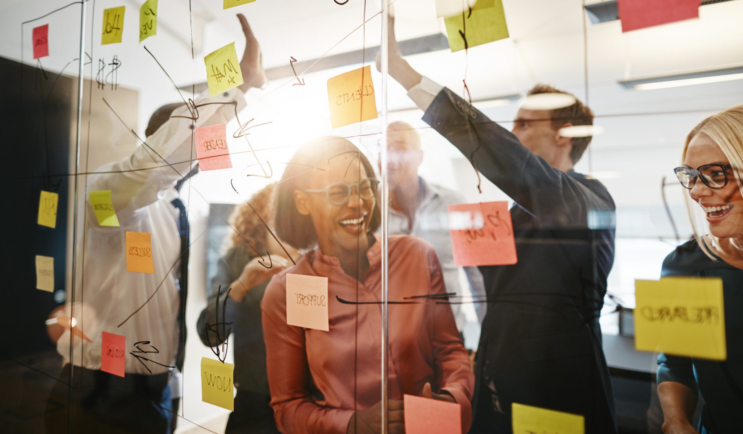 Diverse group of ecstatic businesspeople celebrating a winning idea together while brainstorming on a glass wall in a modern office